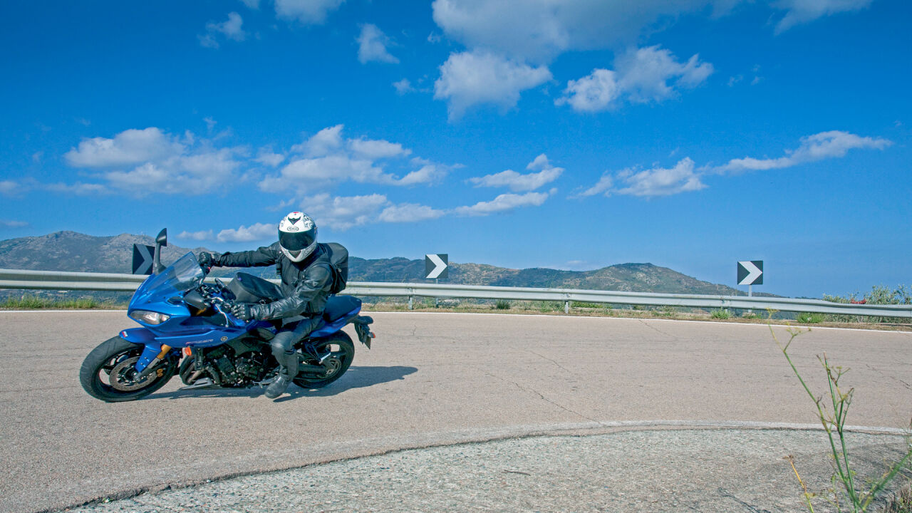 Motorrad in einer Kurve mit Leitplanke, Richtungspfeilen und Bergen im Hintergrund Motorrad in einer Kurve mit Leitplanke, Richtungspfeilen und Bergen im Hintergrund